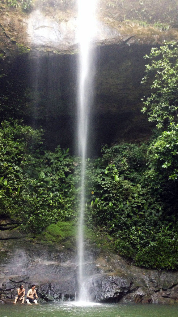 Fotografía de la cascada de la Sierpe cayendo en la piscina natural y unos turistas al lado